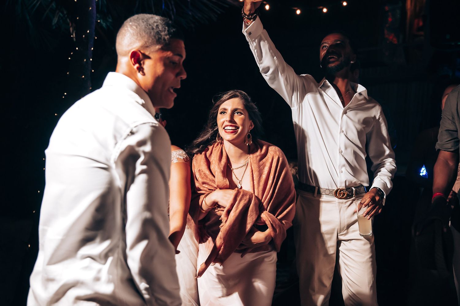 Wedding guests cheer and celebrate during a lively dance floor moment at an evening reception.