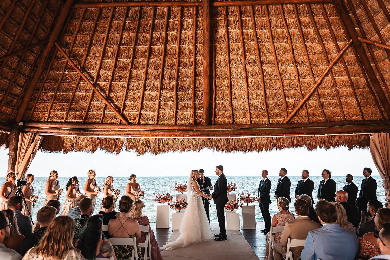 Wedding guests mingle beneath a rustic wooden barn ceiling decorated with twinkling string lights.