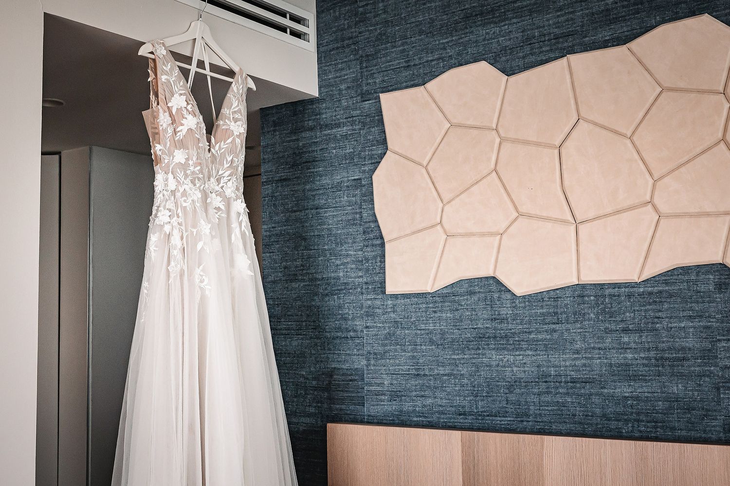White wedding dresses hanging on display against a dark blue textured wall in a bridal boutique.