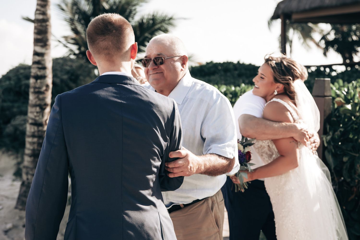Bride and groom greeting family with warm hugs at tropical outdoor wedding ceremony.