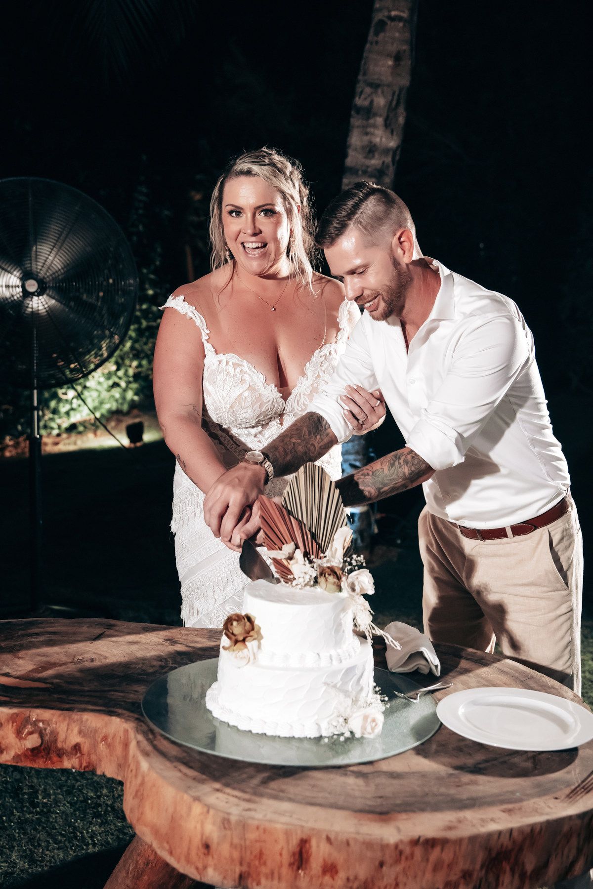 Bride and groom cutting their white wedding cake together outdoors at night.