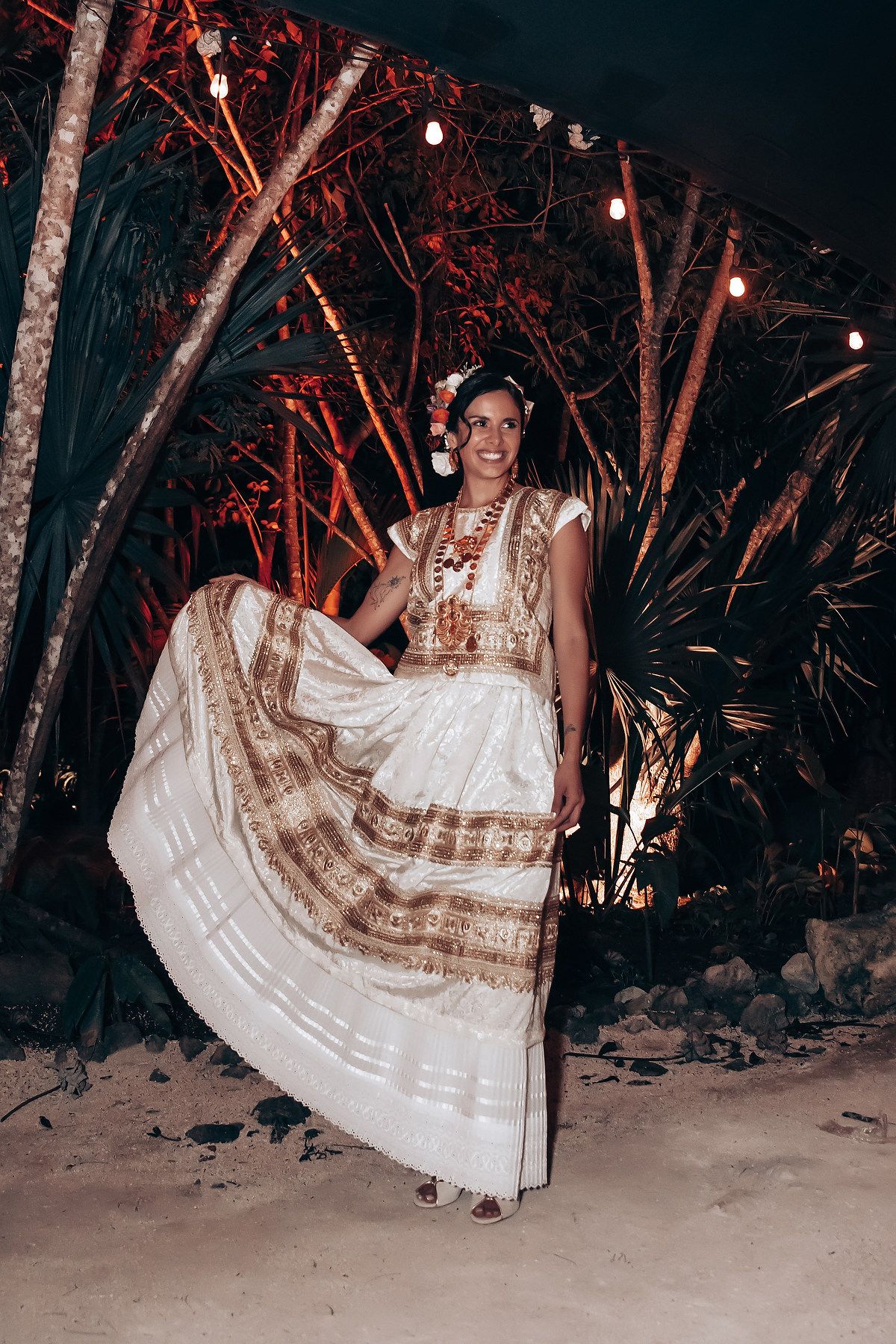 A traditional white and brown patterned dress twirls under string lights at an outdoor celebration.