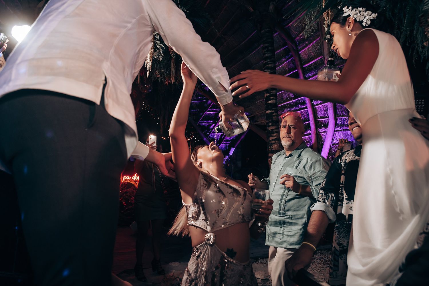 Wedding reception dance floor filled with celebrating guests under purple lighting.