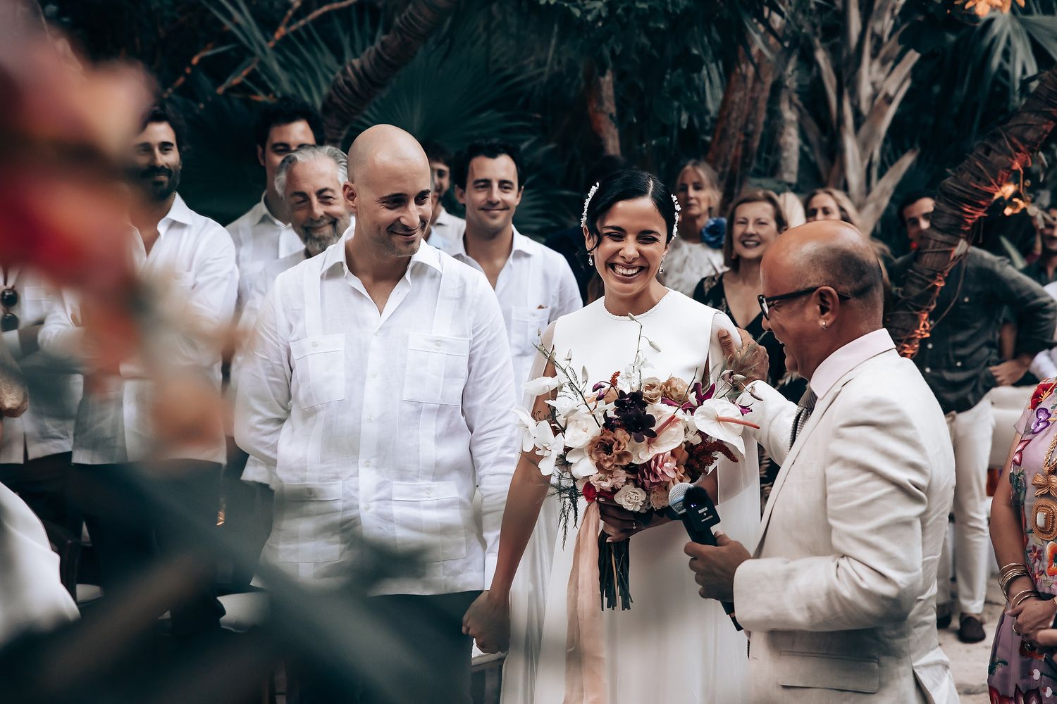 A group of people dressed in white gather outdoors under palm trees at a tropical celebration.