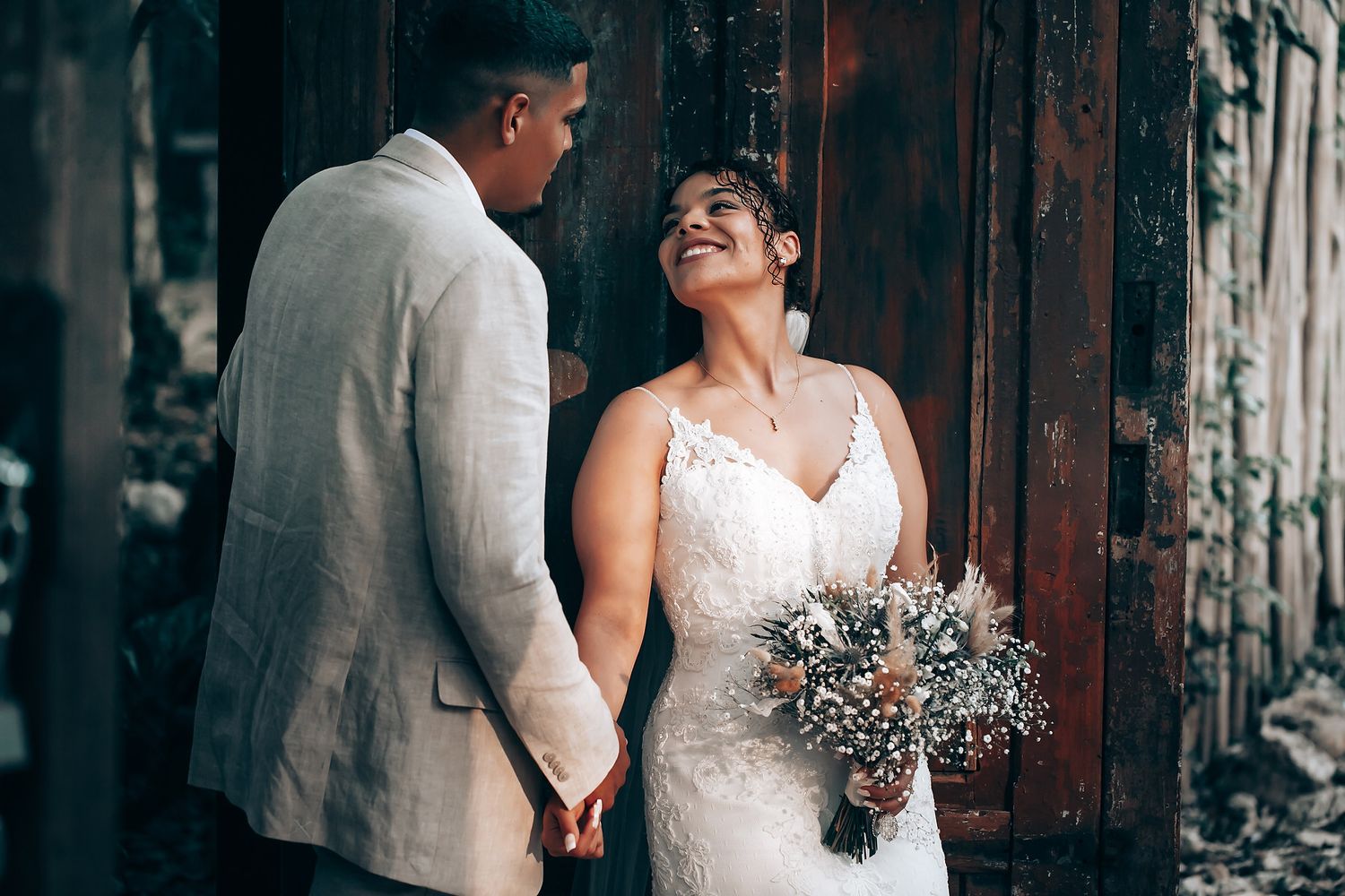 Wedding couple posing against rustic wooden backdrop with natural floral bouquet.