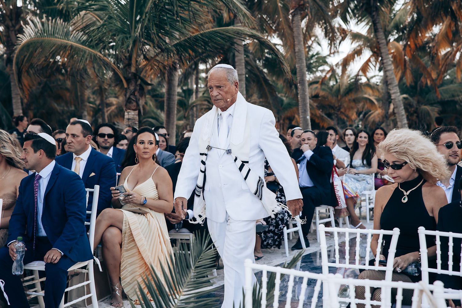 Outdoor wedding ceremony setup with white chairs and tropical palm trees.