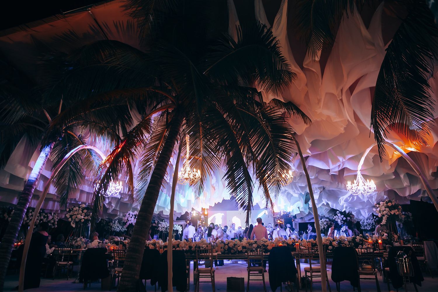 Palm trees silhouetted against colorful evening sky during outdoor wedding reception.