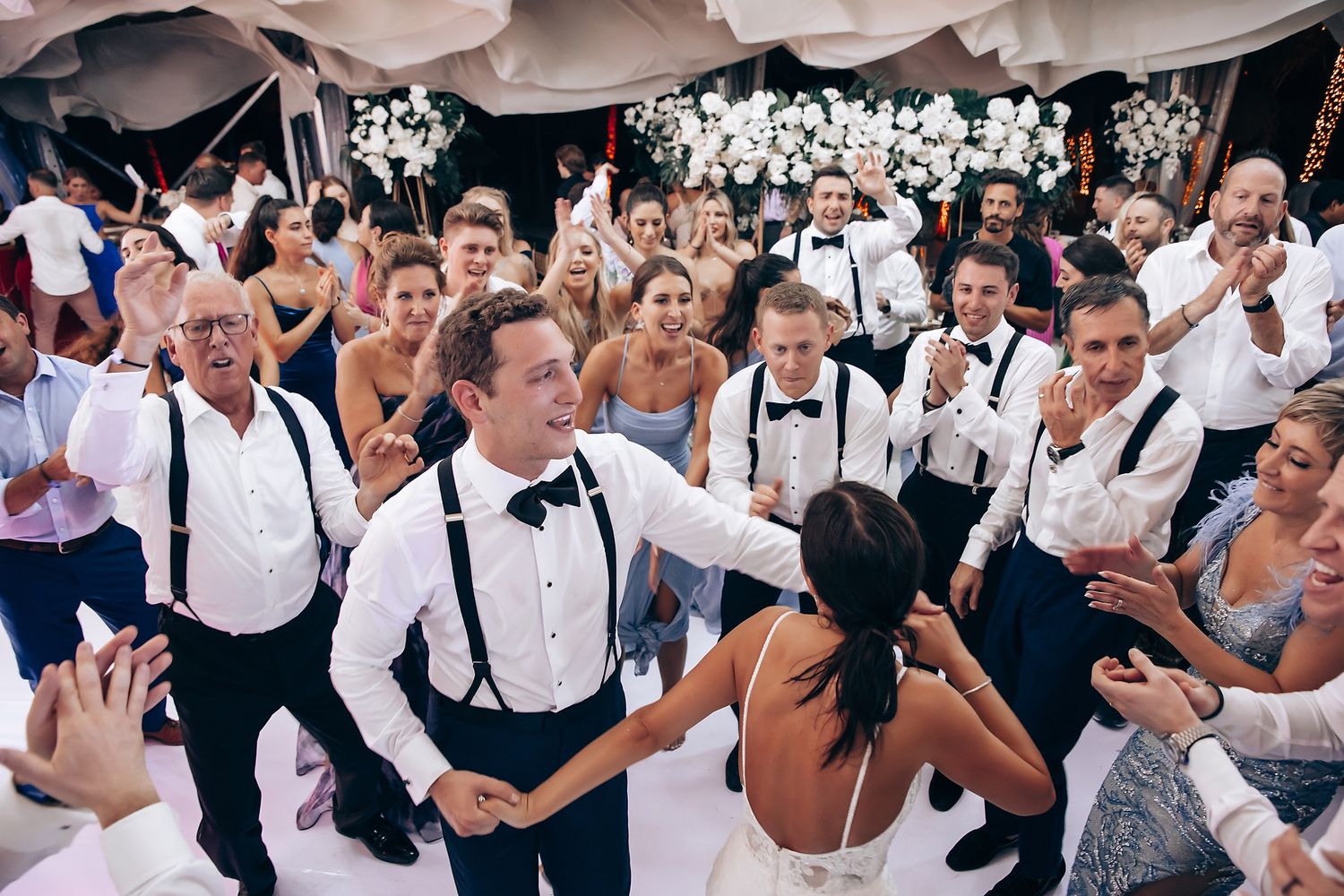 Wedding guests dancing and celebrating on a crowded reception dance floor.
