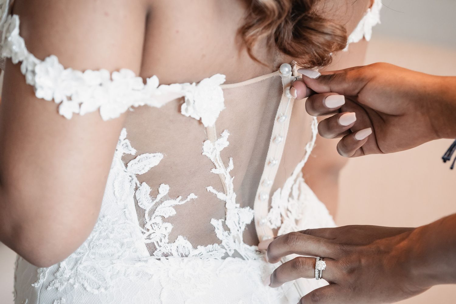Close-up of a bride's lace wedding dress being buttoned up the back.