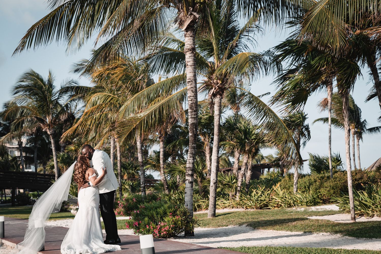 Bride and groom share a romantic moment surrounded by tropical palm trees at a destination beach wedding.