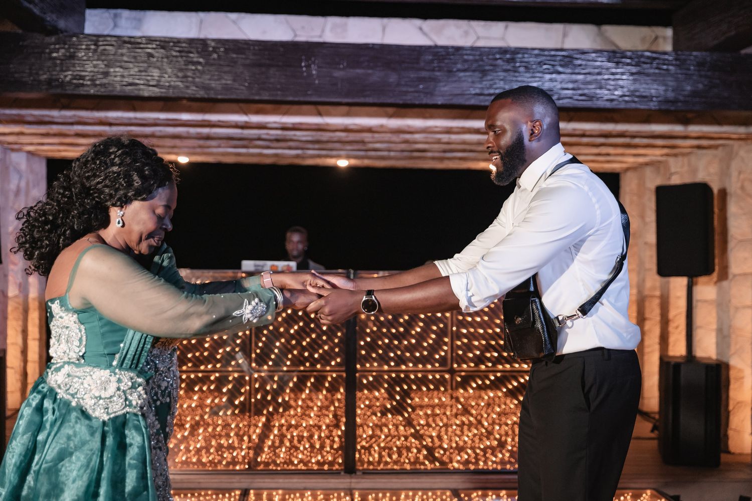 Couple shares a romantic first dance holding hands in front of a glowing candlelit backdrop.
