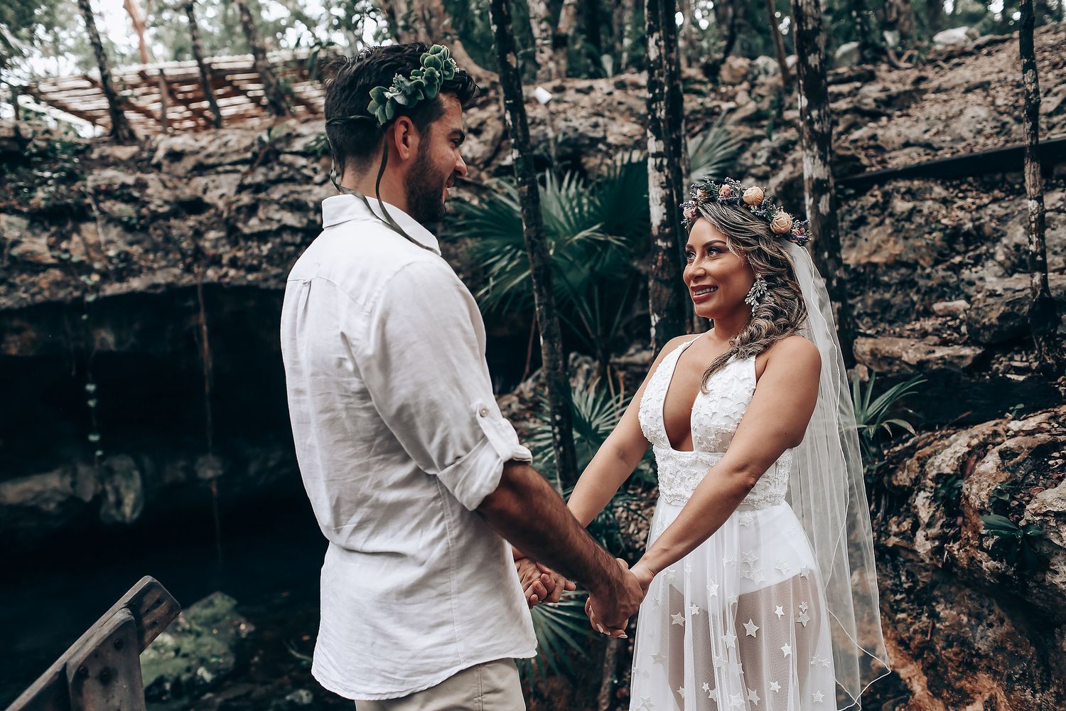 A romantic wedding ceremony takes place in a tropical setting with stone walls and lush greenery.