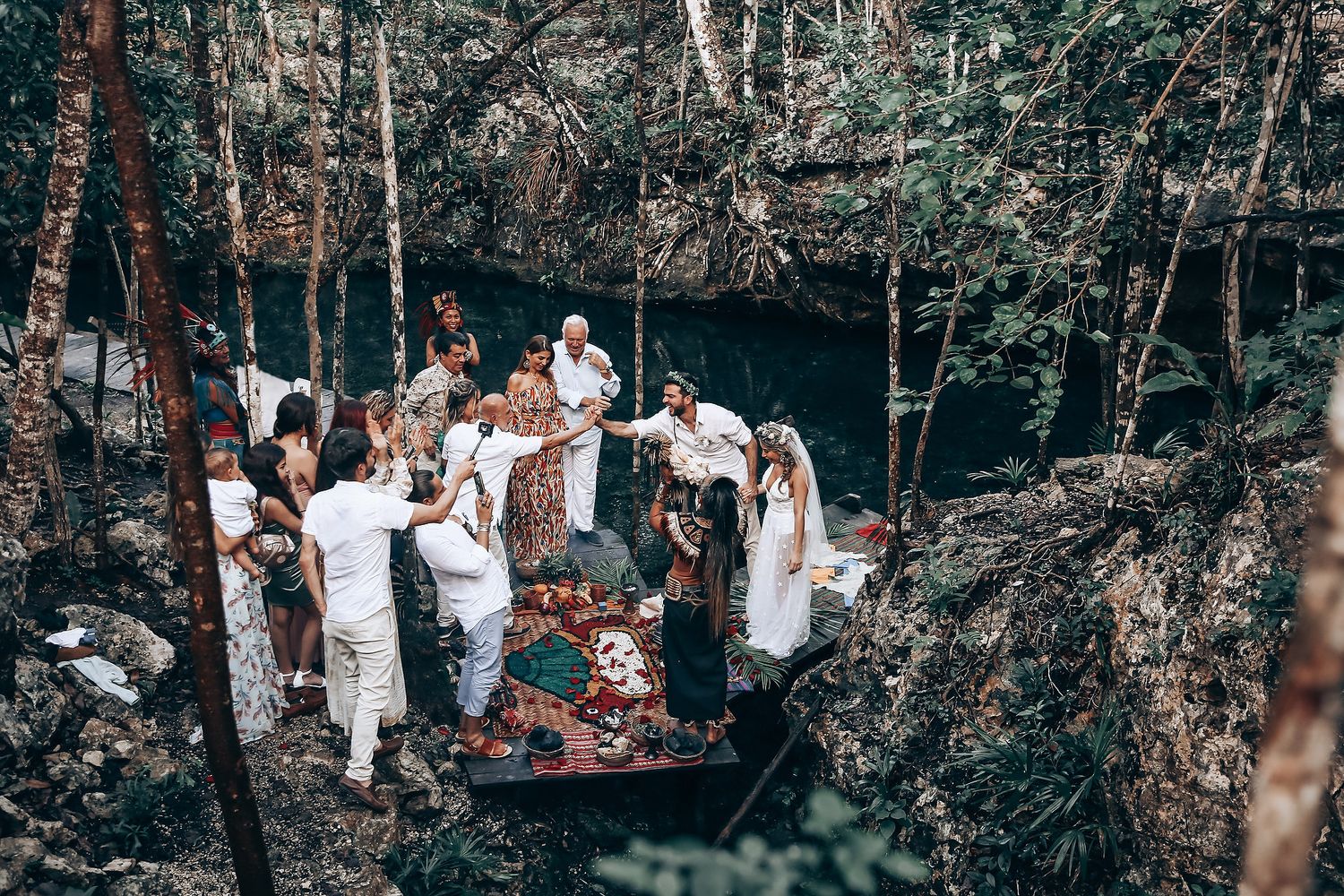 An intimate wedding gathering takes place on wooden platforms surrounded by natural cave walls.