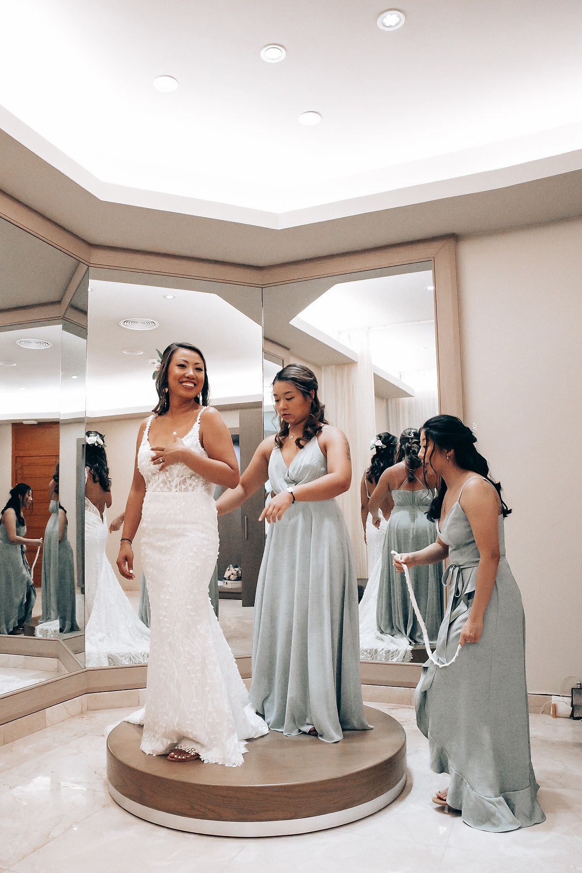 Wedding dress fitting scene in a bridal boutique with mirrors and elegant gowns.