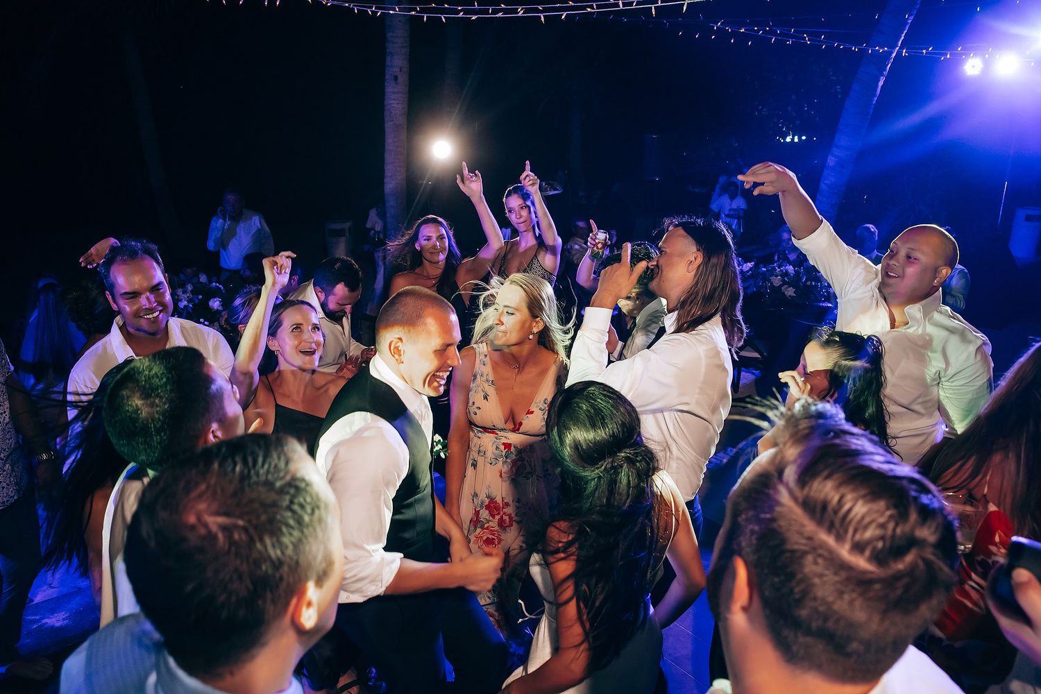 Energetic dance floor scene with party guests celebrating under blue lighting at night.