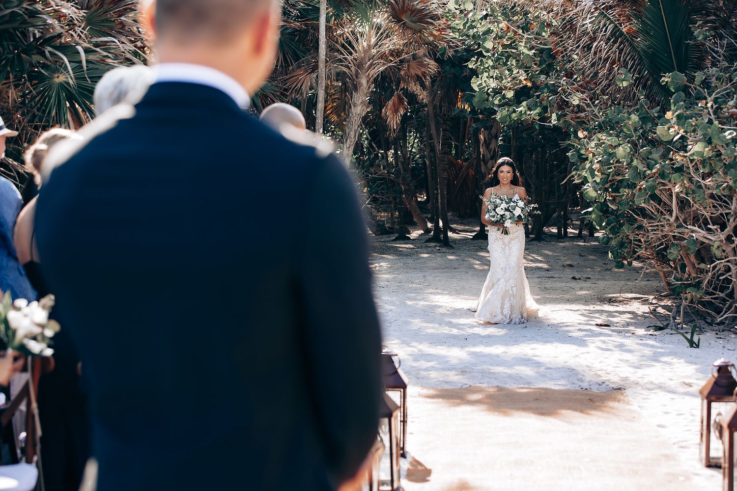 A couple in wedding attire shares a romantic dance outdoors surrounded by guests and lush greenery.