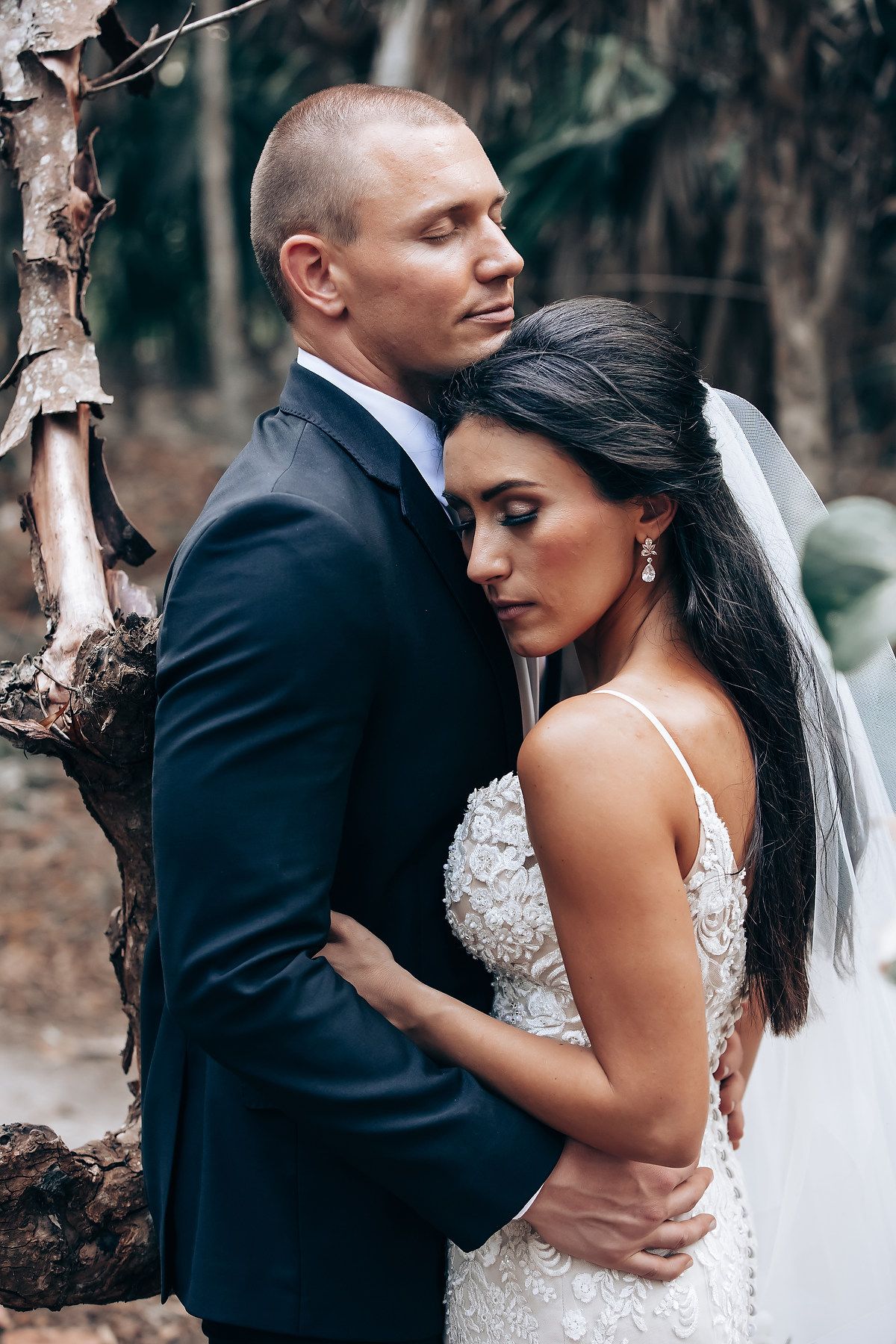 An intimate wedding photo shoot in a wooded area with elegant formal attire and a white veil.