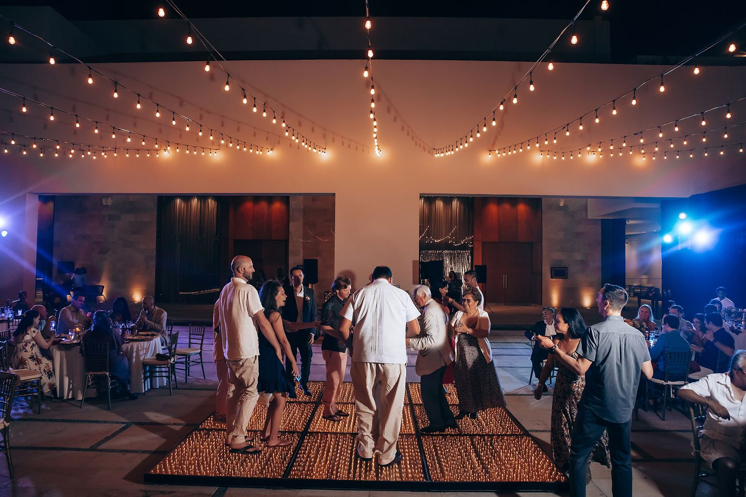 String lights create a magical ambiance over a dance floor at an indoor wedding reception.