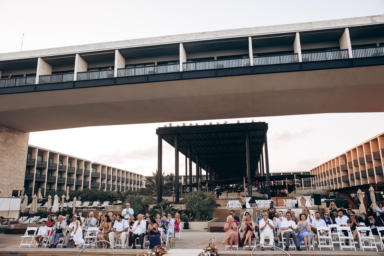 Large modern architectural structure with crowds gathered beneath covered walkways and columns.