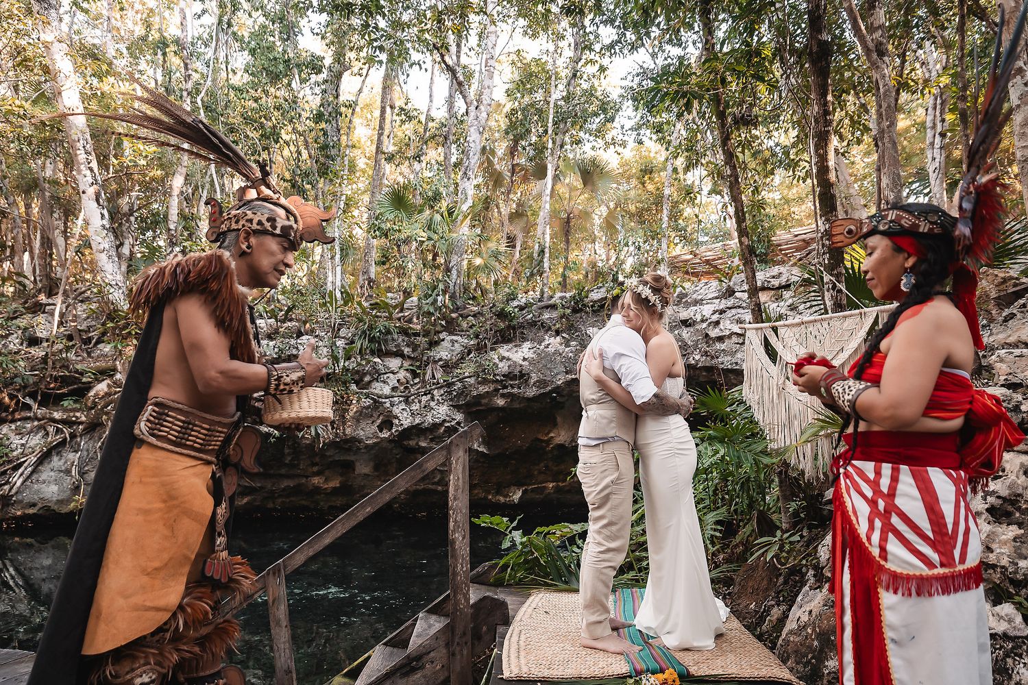 Couple exchanges vows in Mayan ceremony by cenote, officiated by traditional indigenous priests in colorful attire.