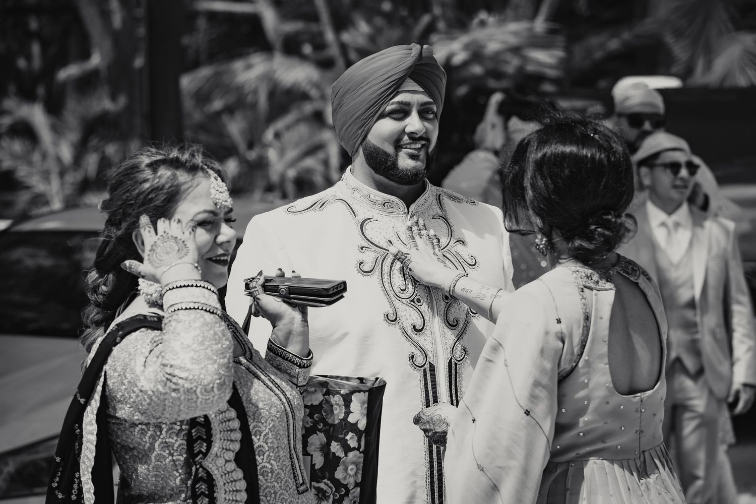 Sikh groom in white sherwani and turban smiling with guests during traditional Indian wedding ceremony.