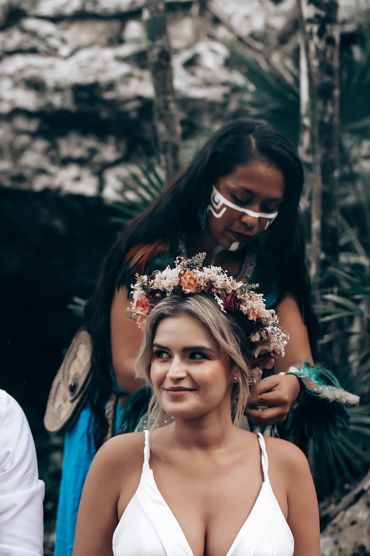 A person wearing a delicate floral crown and white dress poses in a natural outdoor setting.