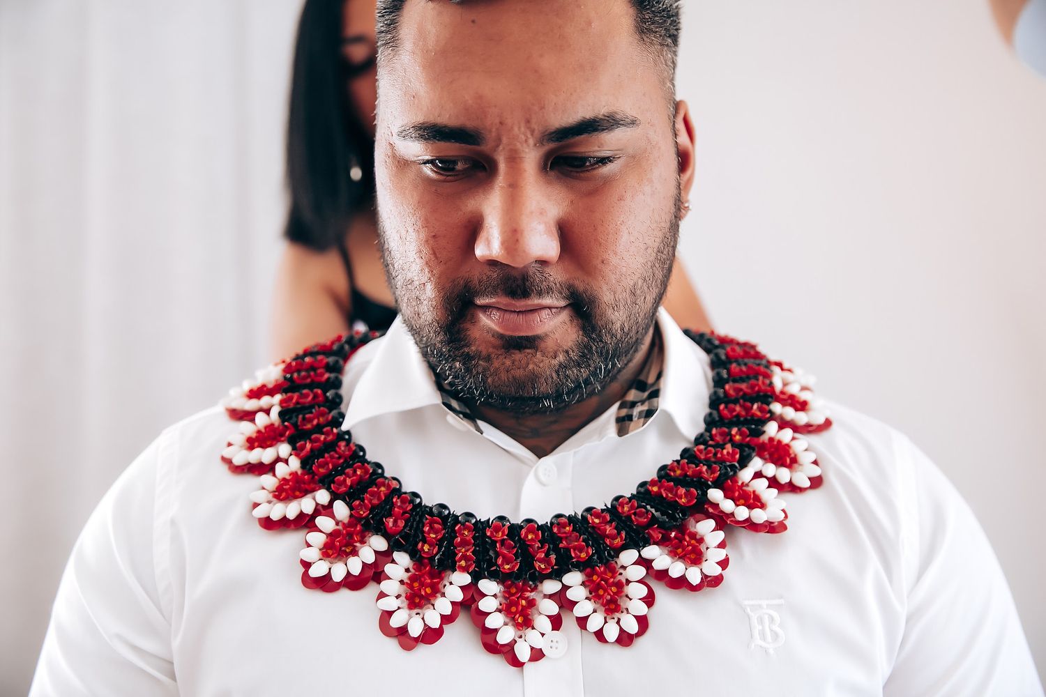 Person wearing a white shirt adorned with a striking red beaded lei necklace.