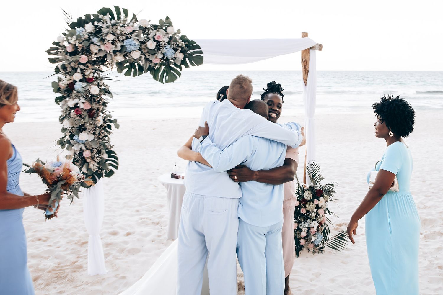 A couple embracing at a beach wedding ceremony with a floral arch in the background.