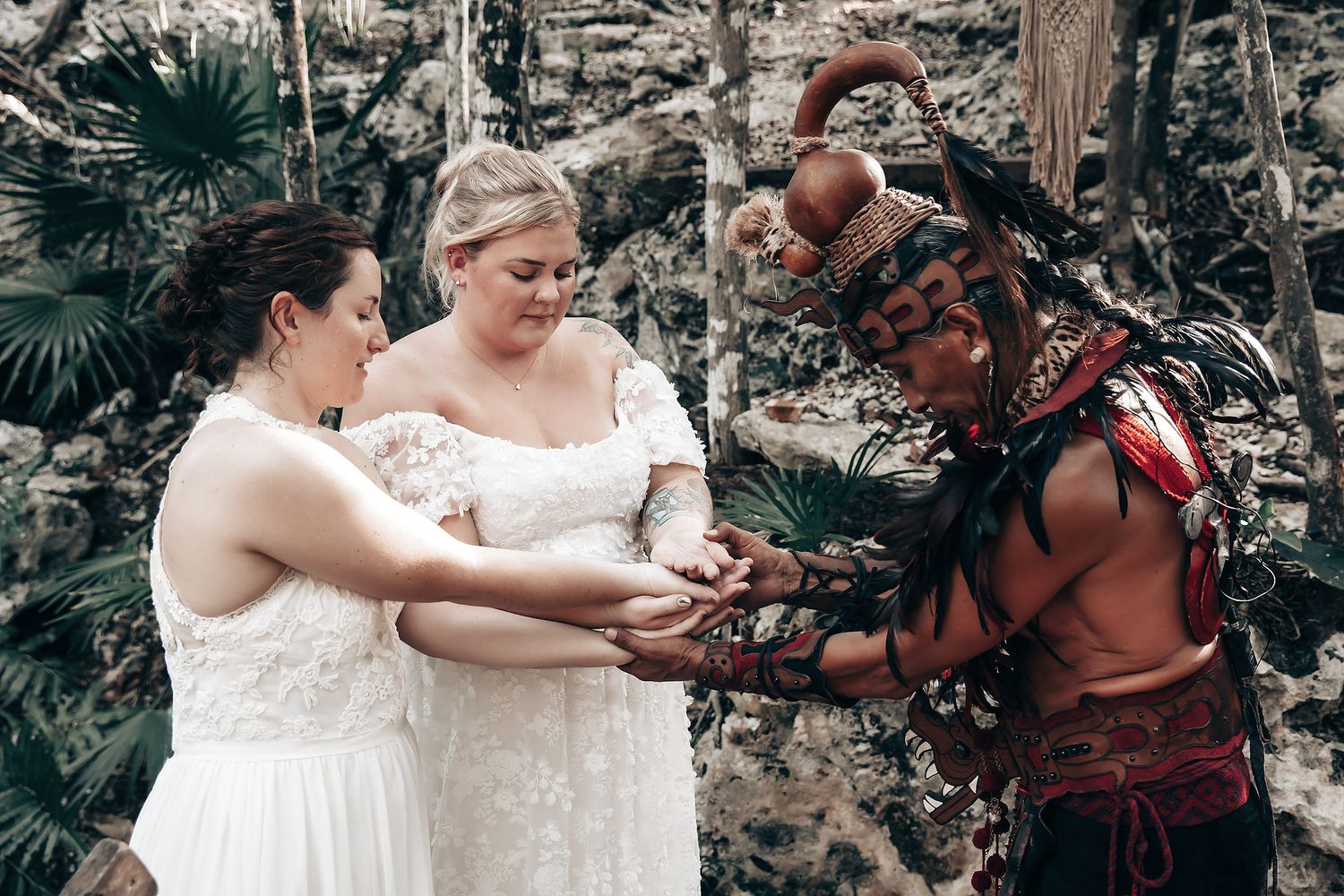 Two brides embracing in a lush, natural setting.