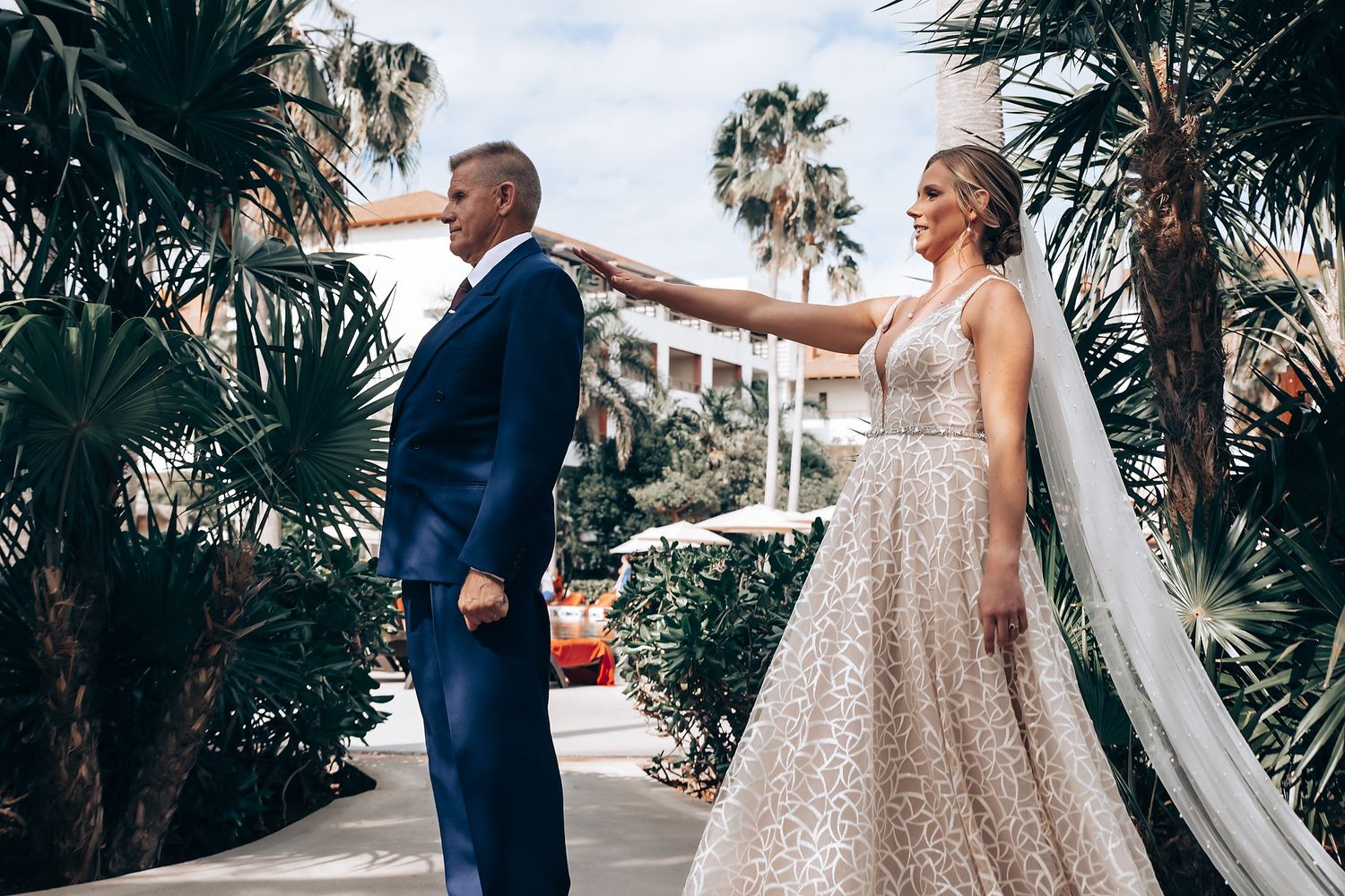 A bride and groom standing together in a tropical setting with palm trees in the background.