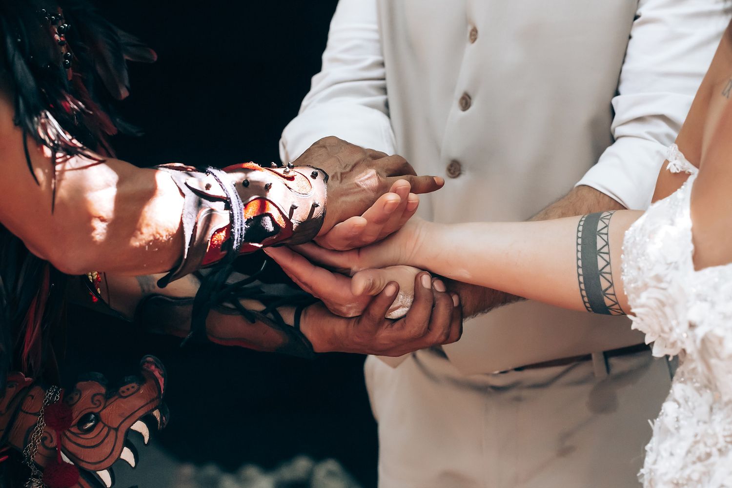 Hands joining together during wedding ceremony with white dress visible in background.
