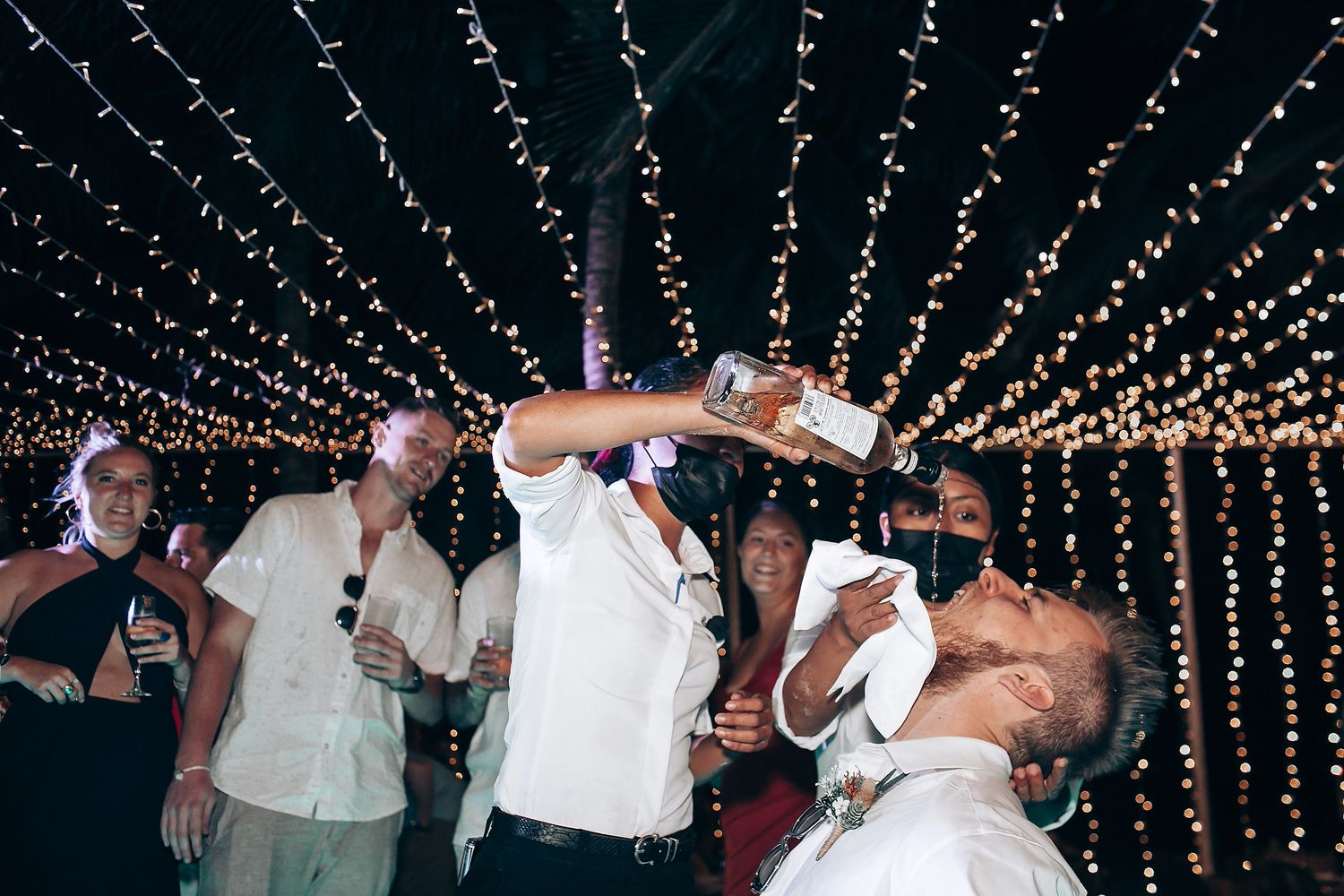 Wedding party dancing and celebrating under a canopy of warm fairy lights at an evening reception.