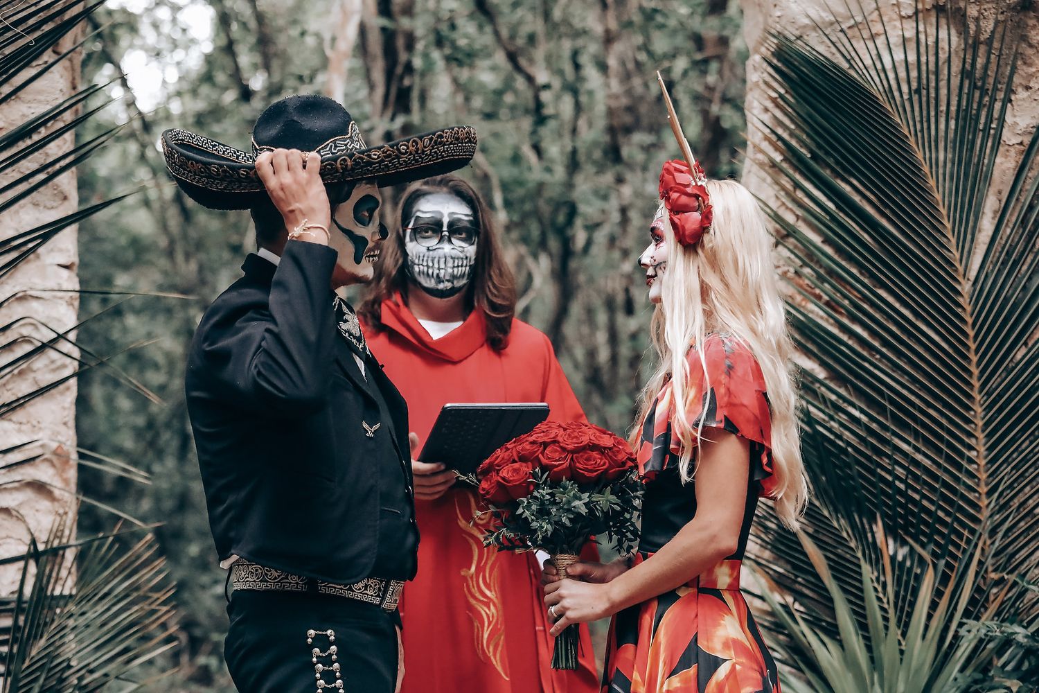 Forest wedding ceremony with gothic elements and red floral arrangements.