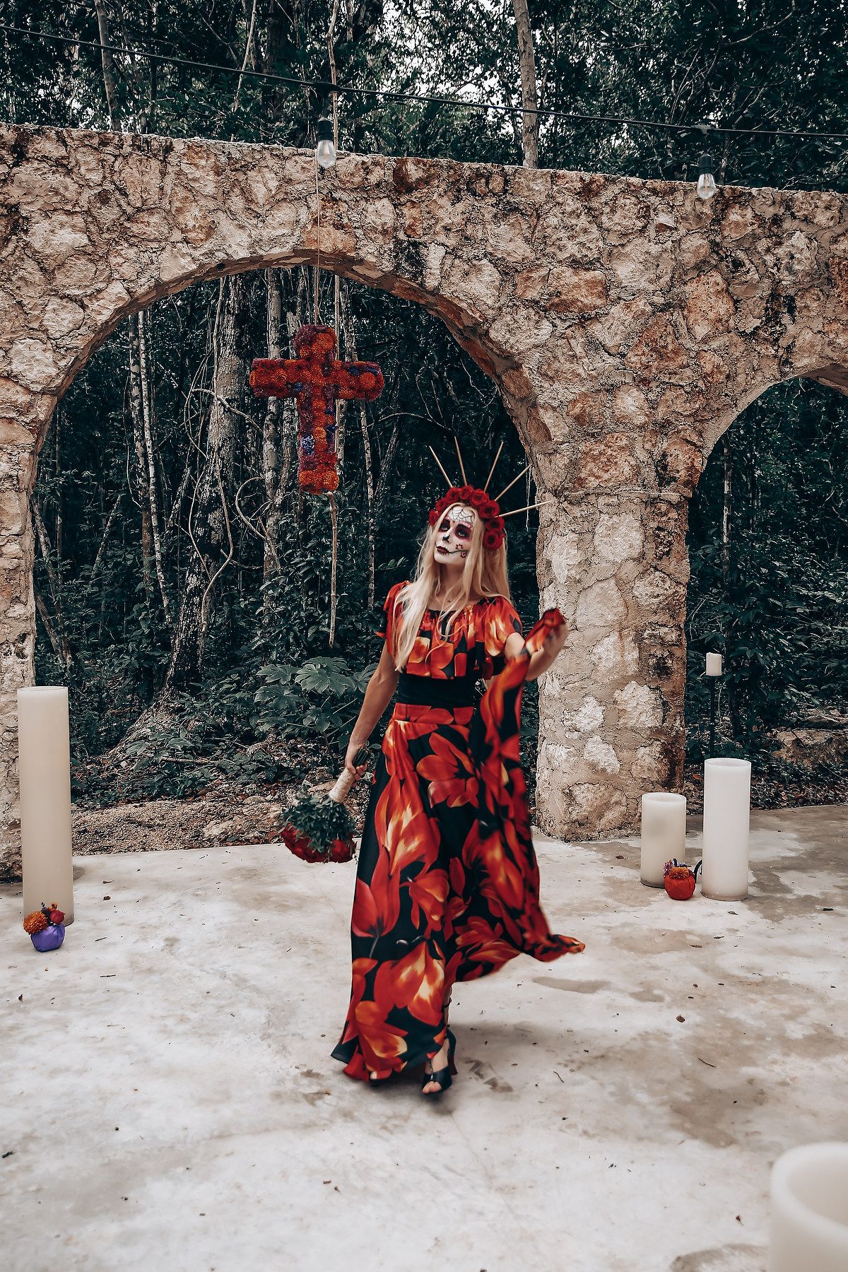 Gothic-styled wedding scene with red cross and dramatic floral dress against stone archway.