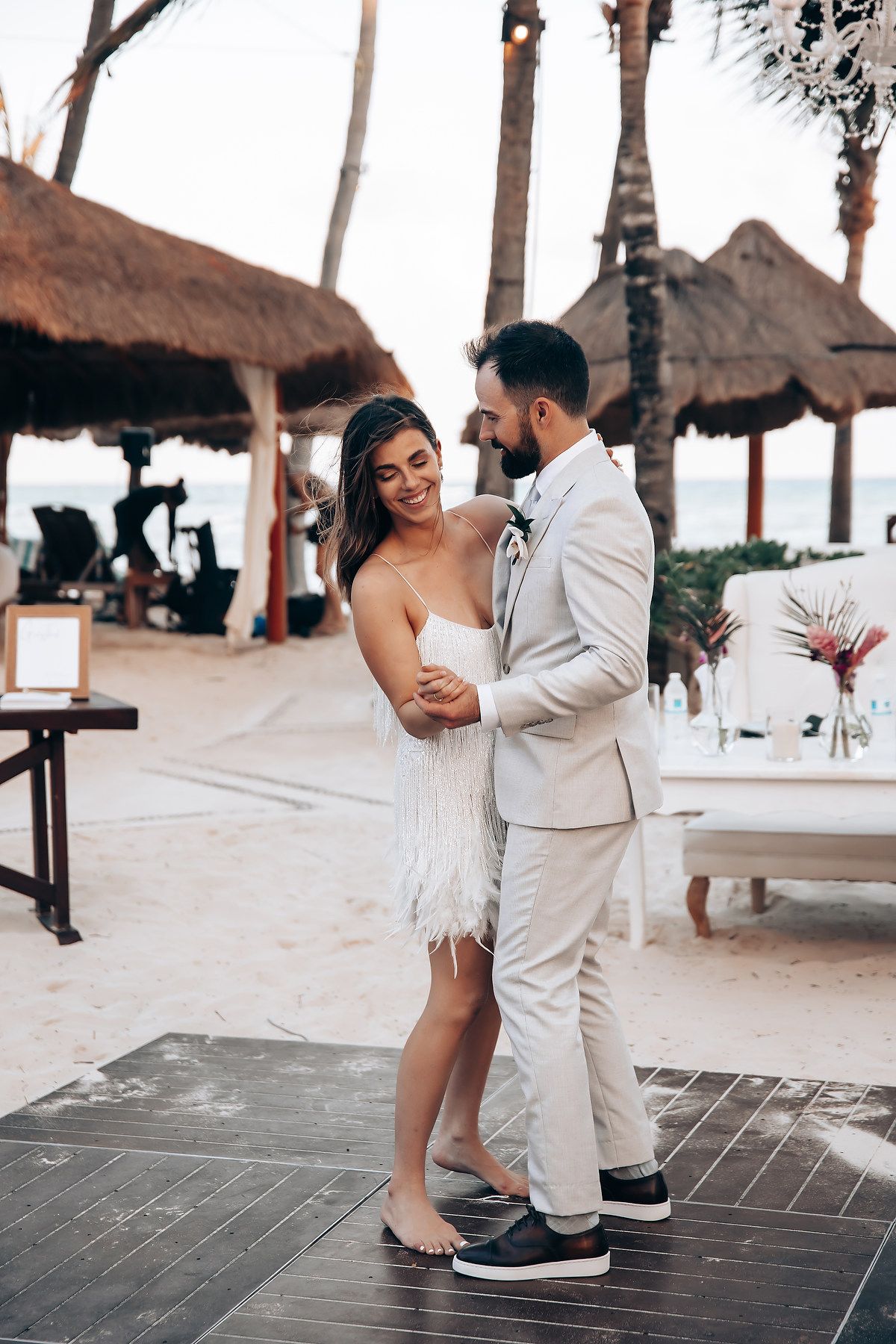 A couple dances together on a beachfront deck under thatched palapas.