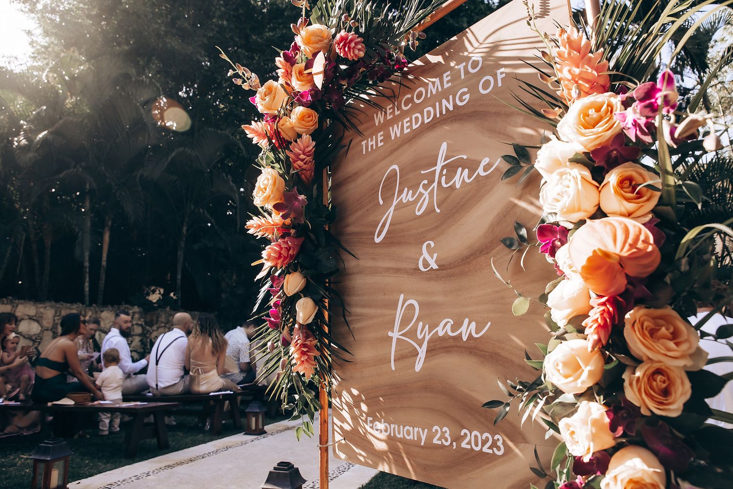 Wooden wedding welcome sign decorated with peach and coral floral arrangements.