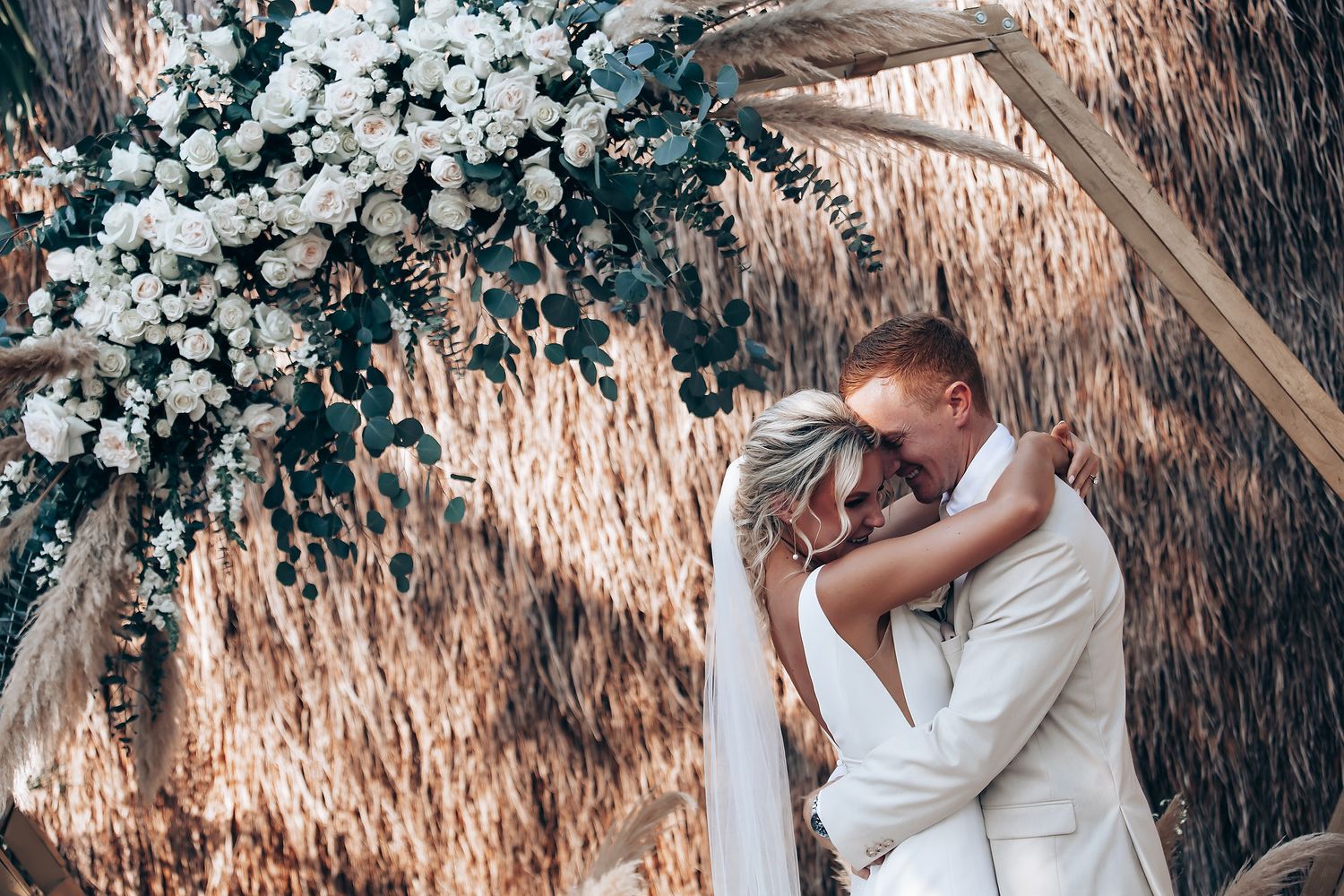Wedding couple embraces near white floral arrangements and natural decor.