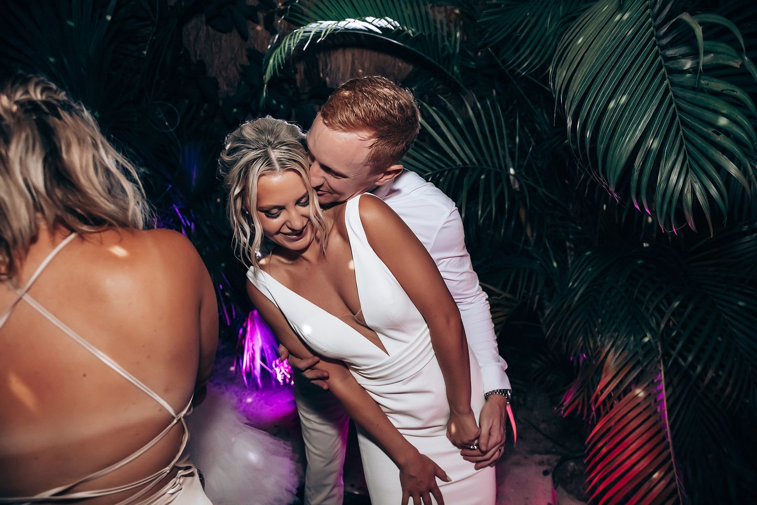 Guests dancing and celebrating at a dimly lit wedding reception with tropical decor.