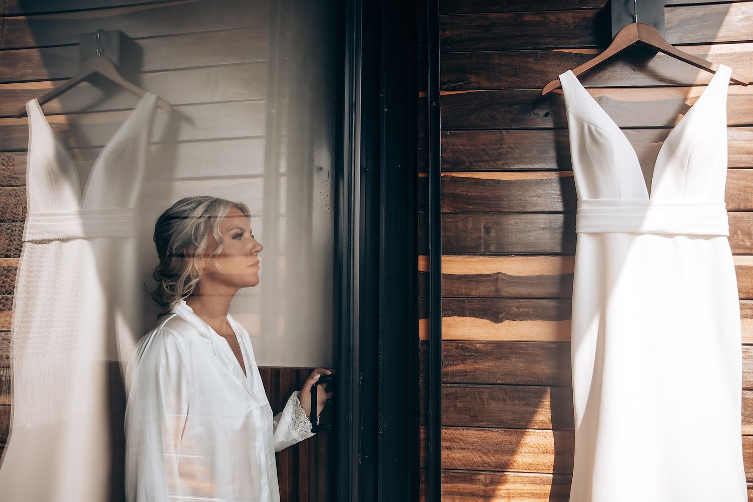 White wedding dresses hanging in a row against rustic wooden walls in a bridal boutique interior.