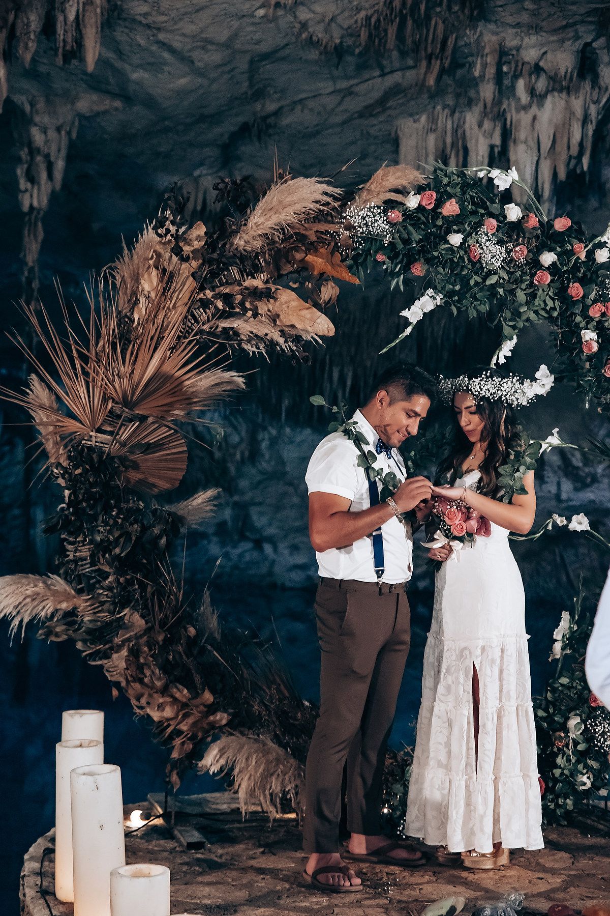 A romantic cave elopement ceremony with dried palm leaves and white candle decor creates an intimate atmosphere.