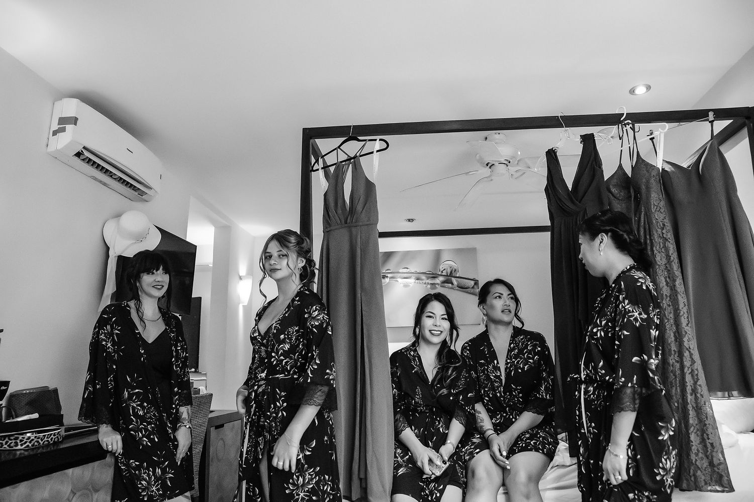 A group in matching sequined robes share laughter while getting ready in a dressing room with hanging garments.