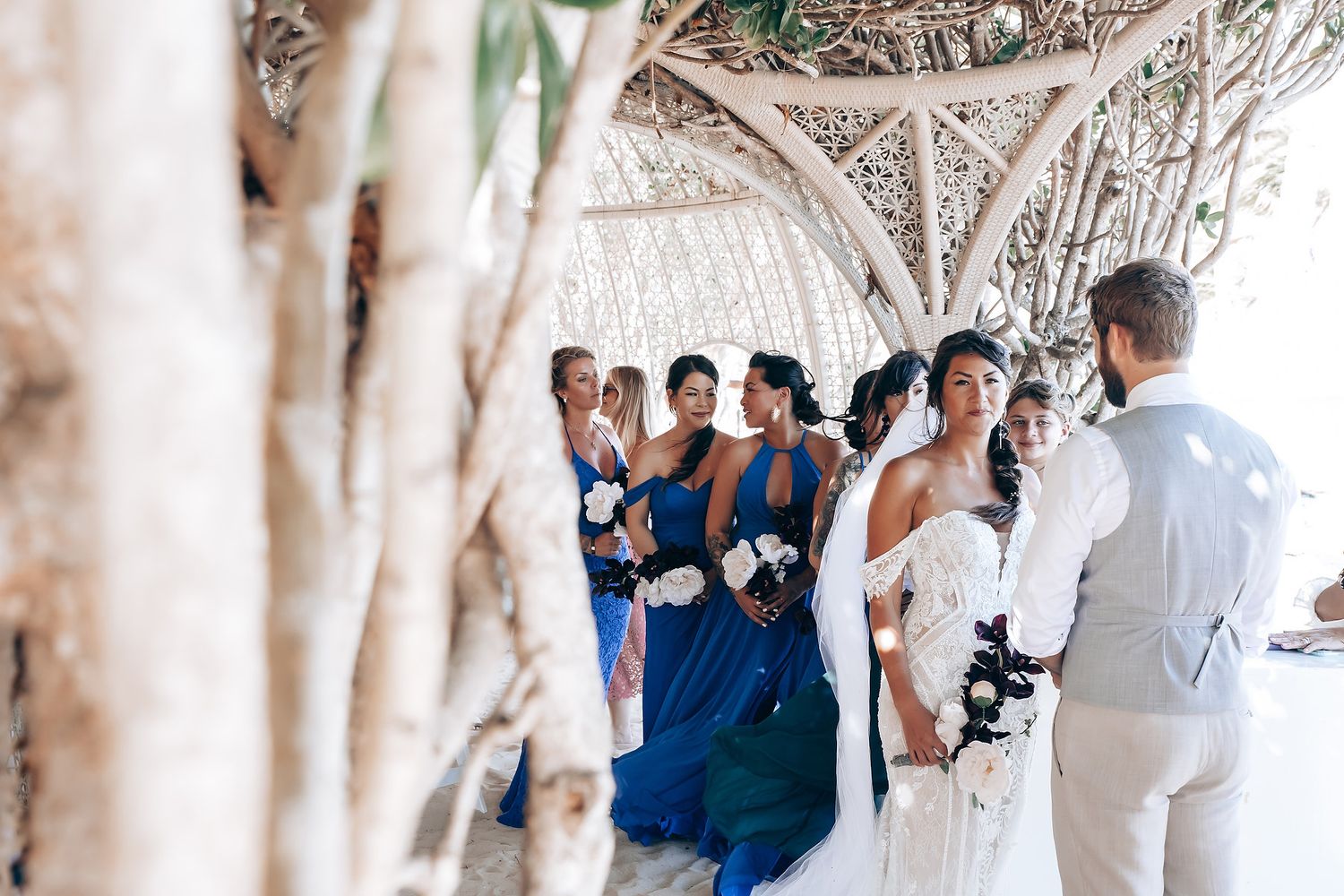 Wedding guests celebrate under a canopy of trees along a white sandy pathway.