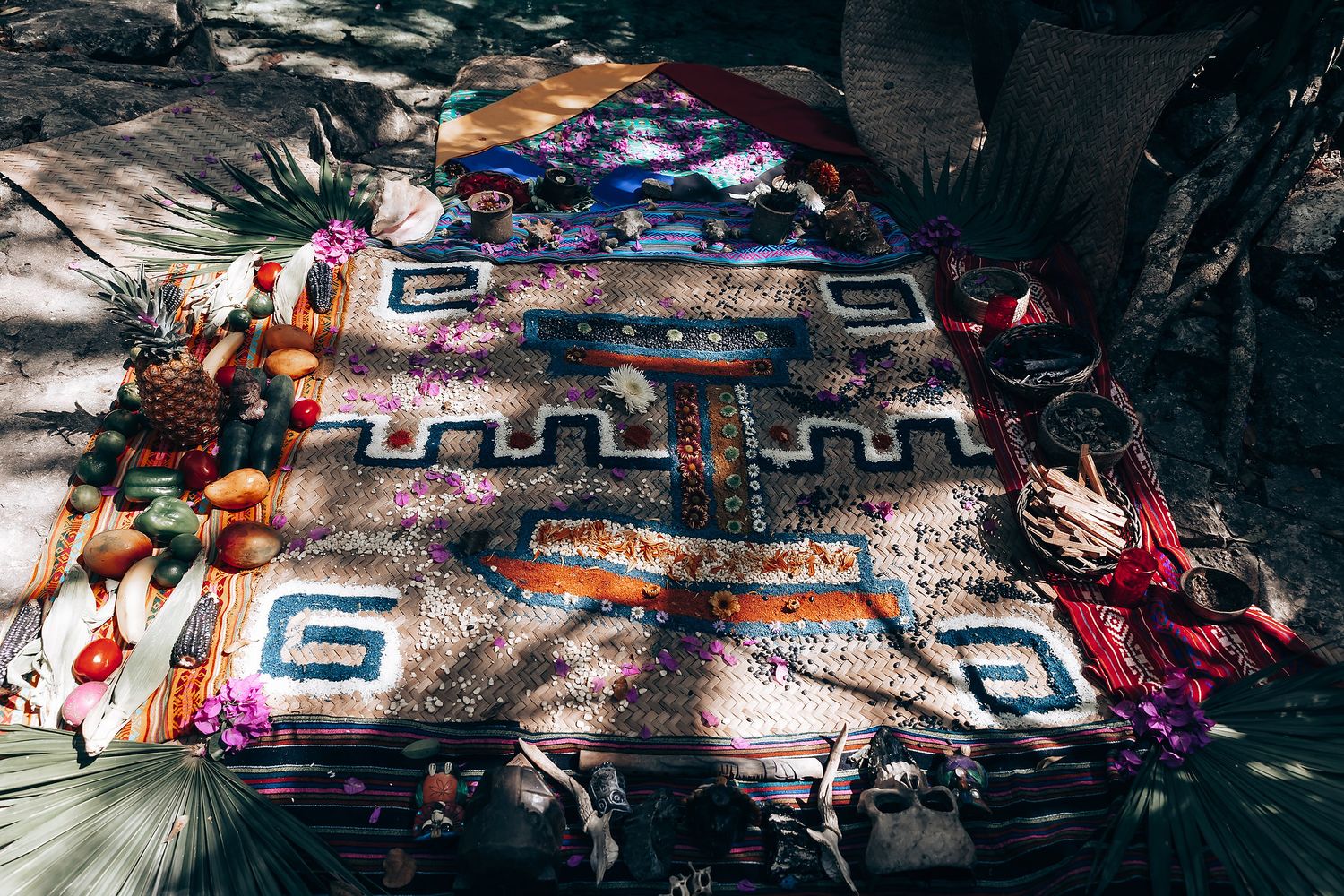 Colorful tribal rug with geometric patterns laid out on ground with scattered clothing and items around it.