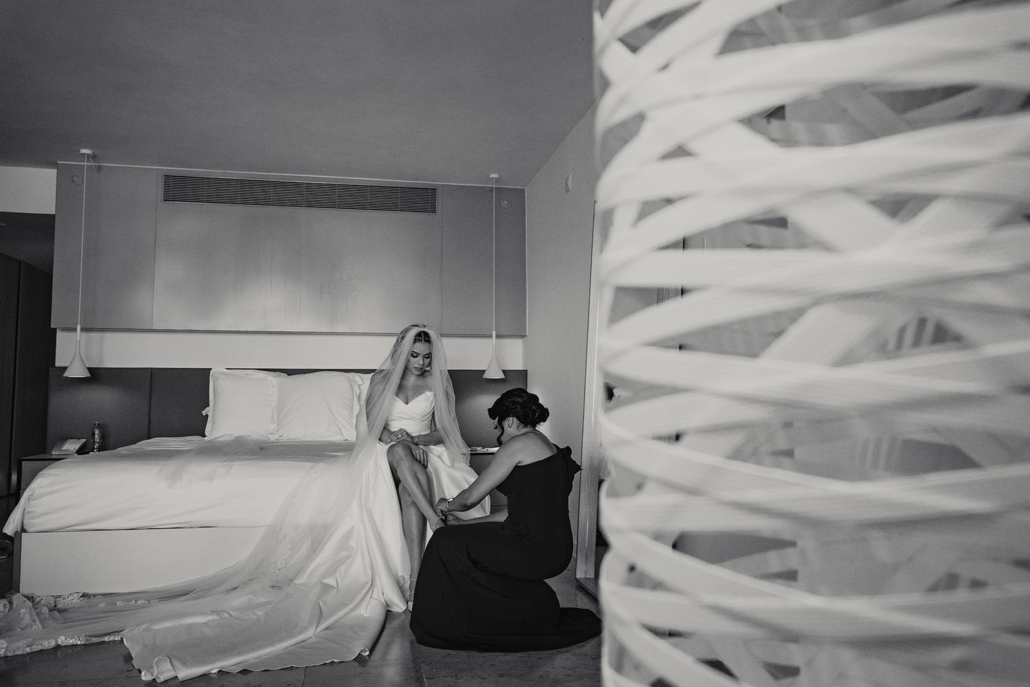 Bride in wedding dress being helped by bridesmaid in hotel room.
