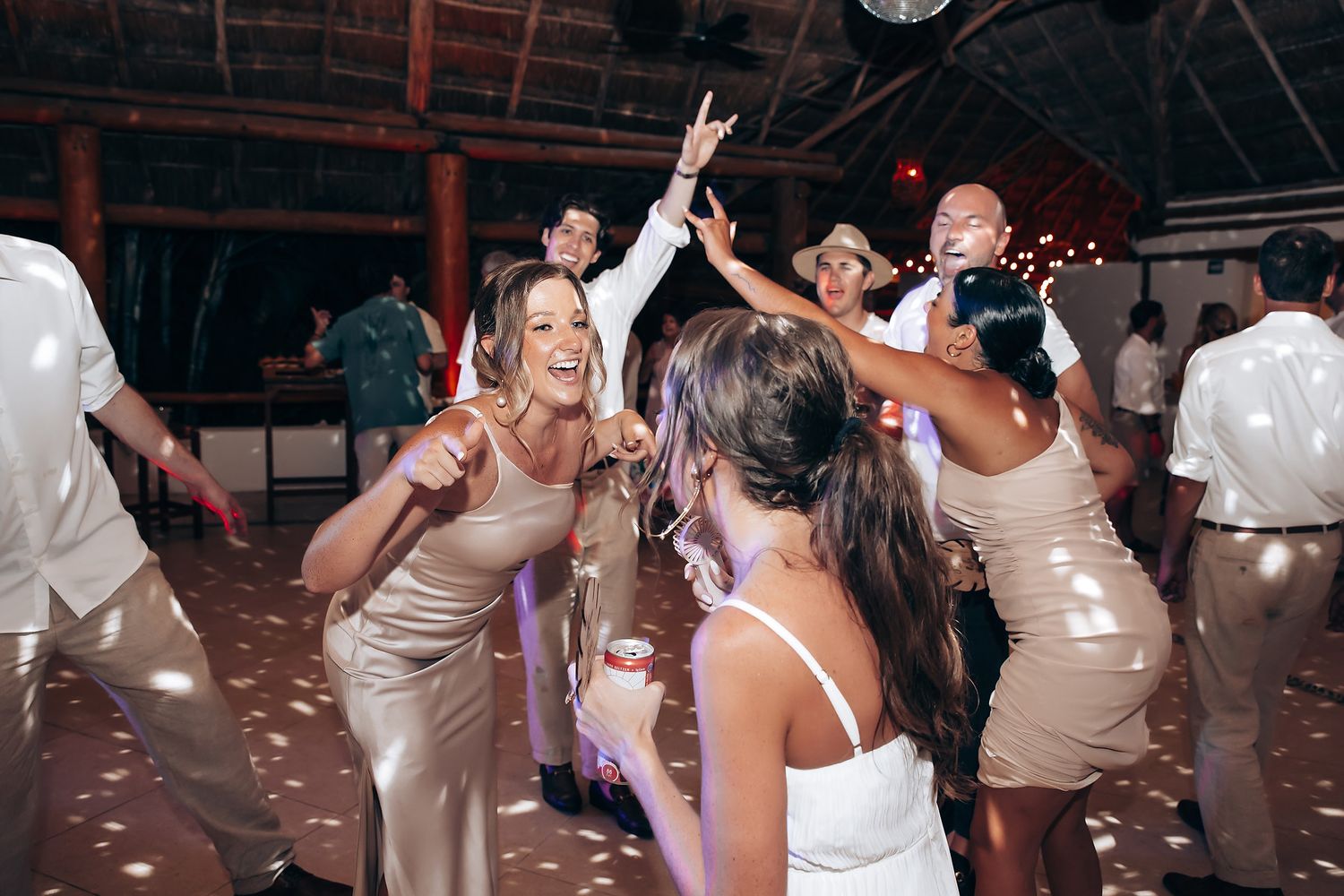 Energetic wedding reception dance party with guests in champagne-colored dresses.