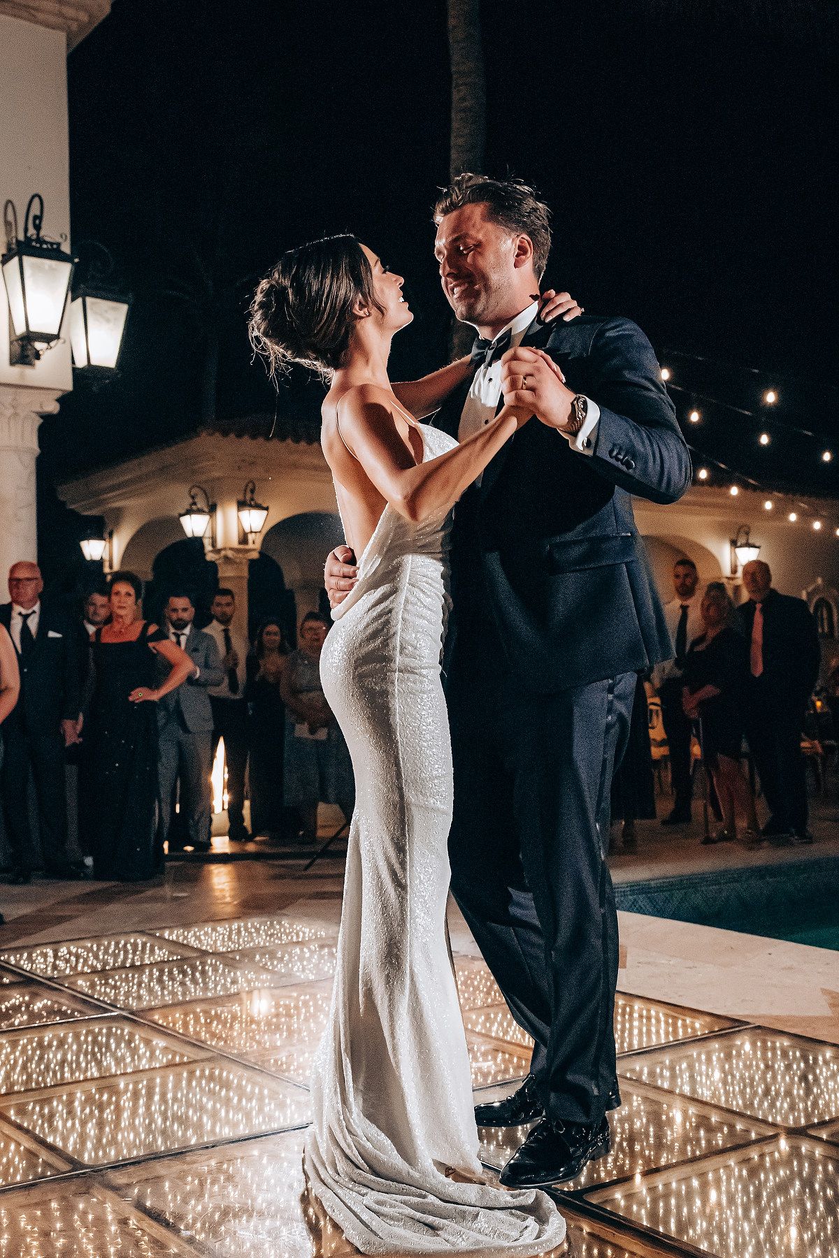 Couple sharing their first dance under romantic string lights at an evening reception.