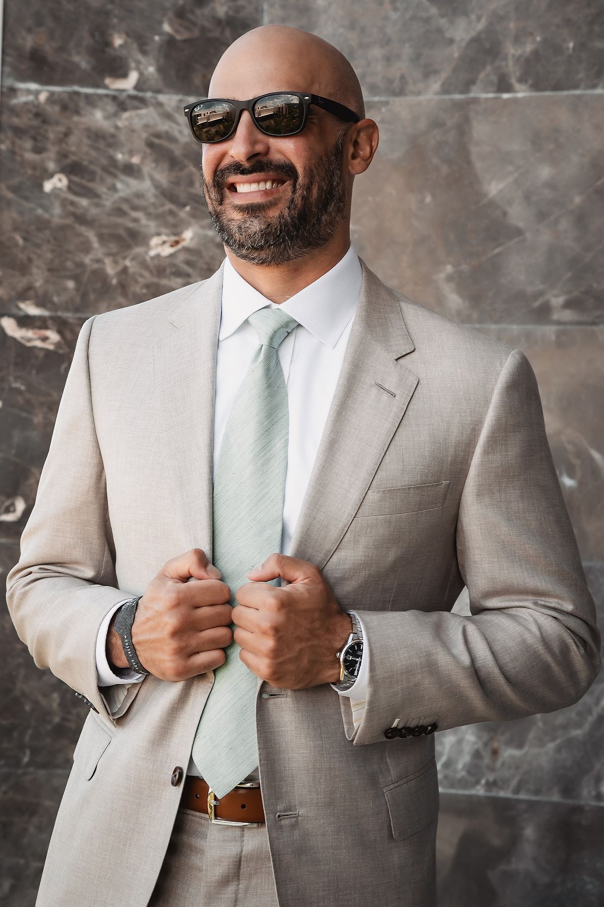 A groom in a light gray suit and mint tie adjusts his jacket while smiling in a series of candid shots.