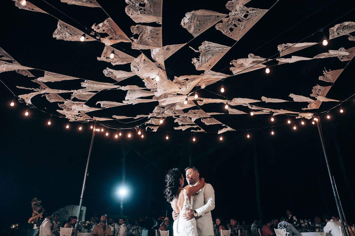 String lights illuminate an outdoor reception venue with a canopy overhead creating a magical atmosphere.