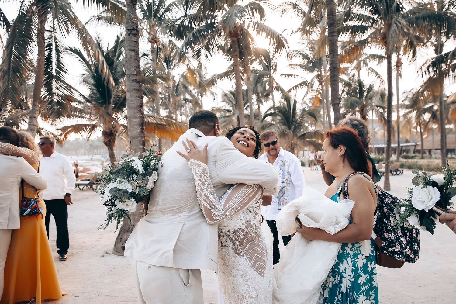 Wedding party dancing and celebrating on a tropical beach with palm trees at sunset.