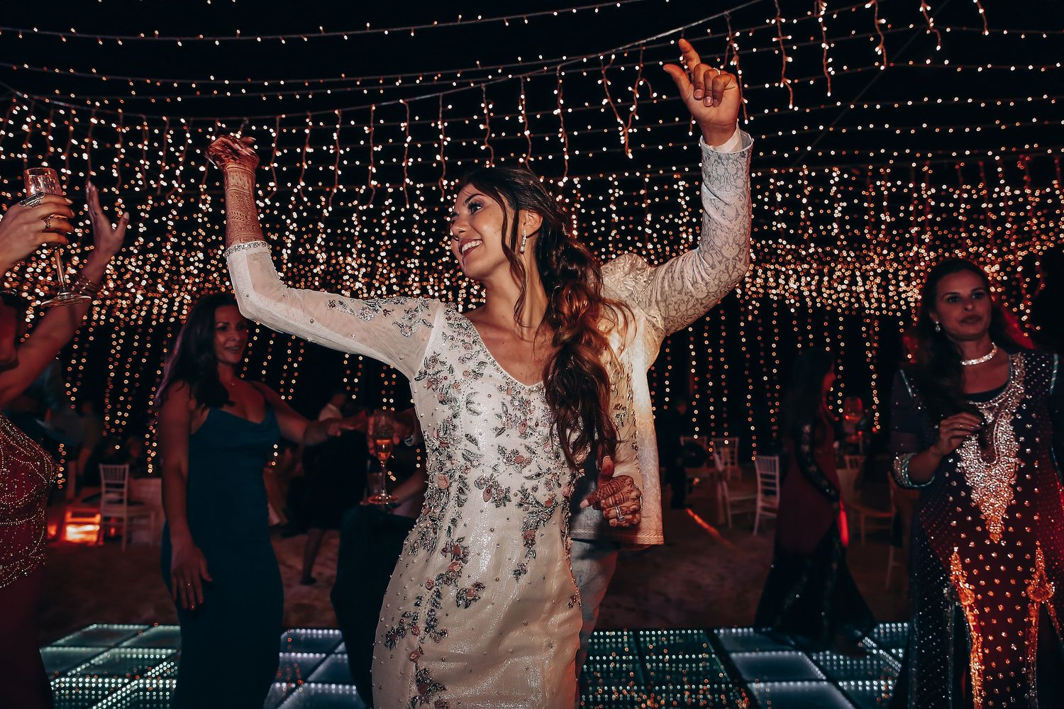Wedding guests dancing and celebrating under a canopy of twinkling string lights at an evening reception.